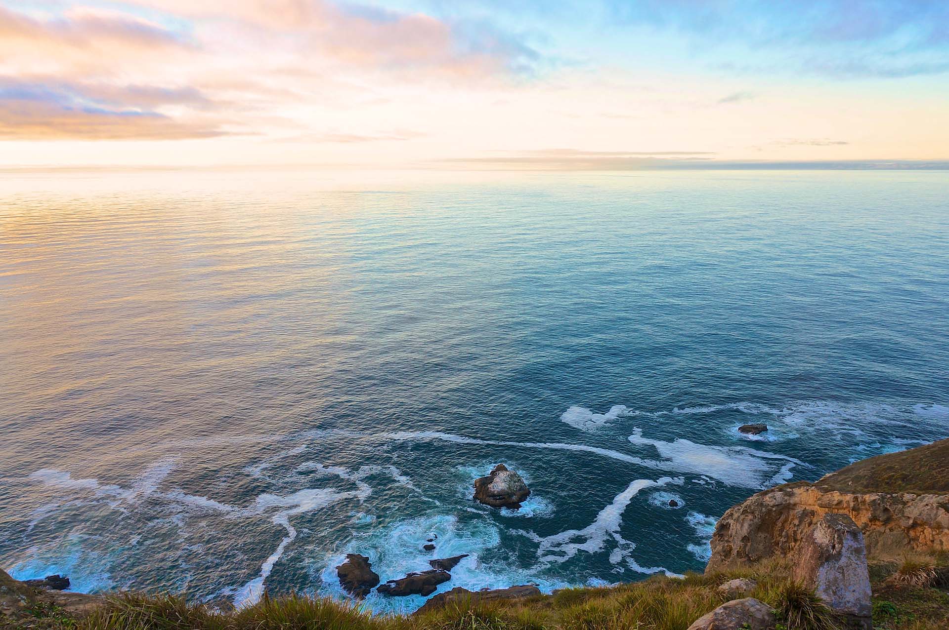 An aerial view of cliffs, rocks and the ocean at sunrise.
