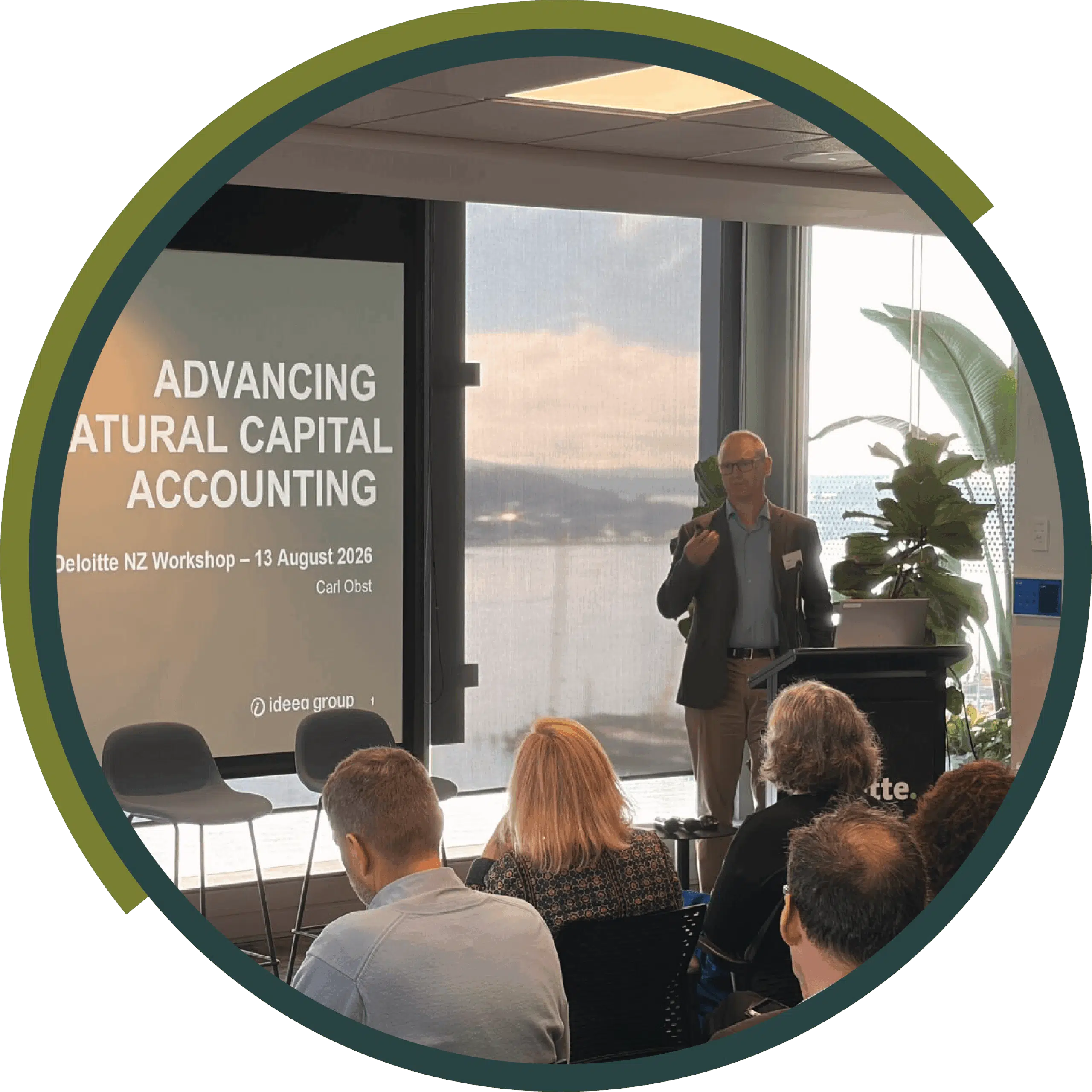 Carl Obst speaking to a seated audience beside a screen titled “Advancing Natural Capital Accounting”