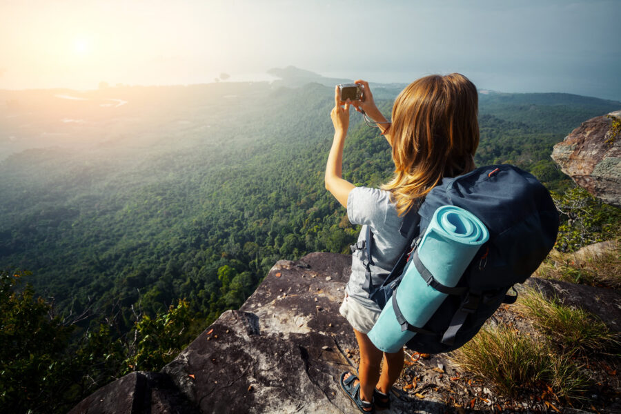 A hiker is standing on a rocky outcrop taking a photo.