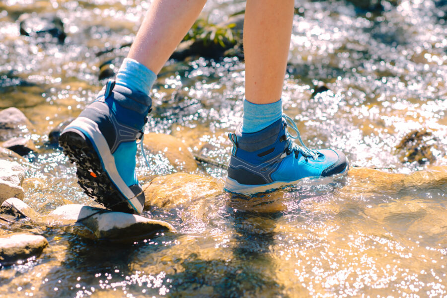 A person in blue hiking boots walking through a rocky creek