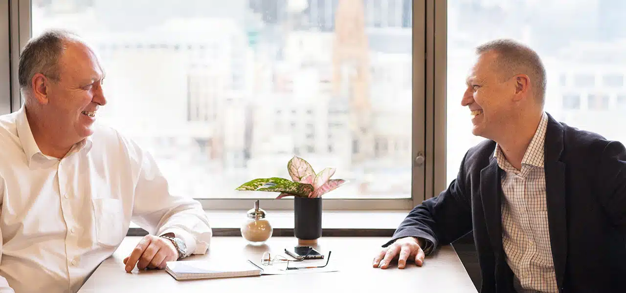 IDEEA group founders, Mark and Carl in conversation at a table by a window overlooking the city