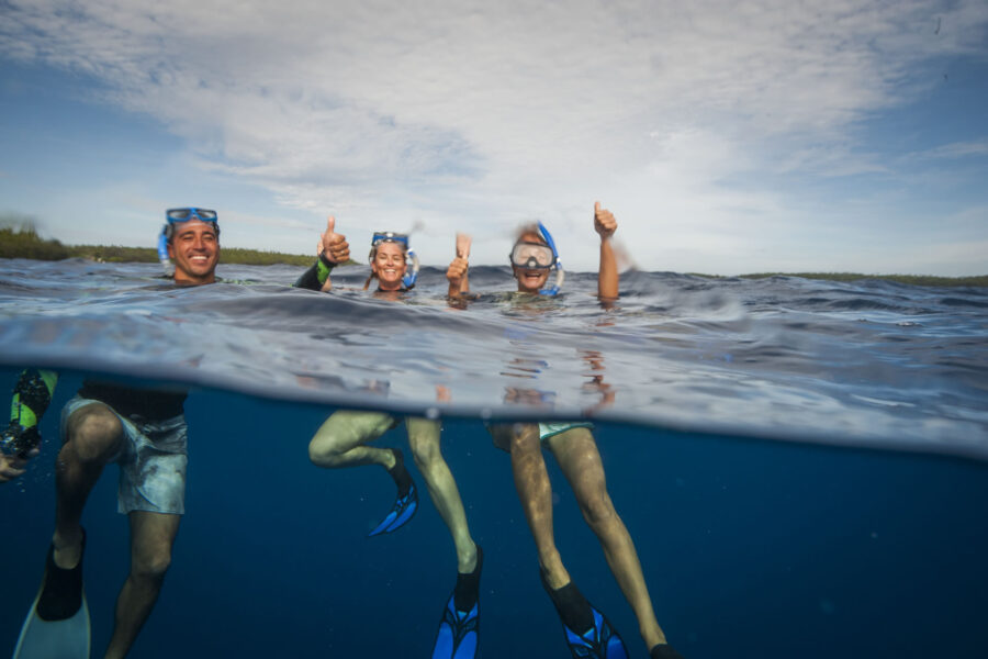 Three people are snorkelling in the water in Tonga. They are smiling and making thumbs up gestures for the camera.